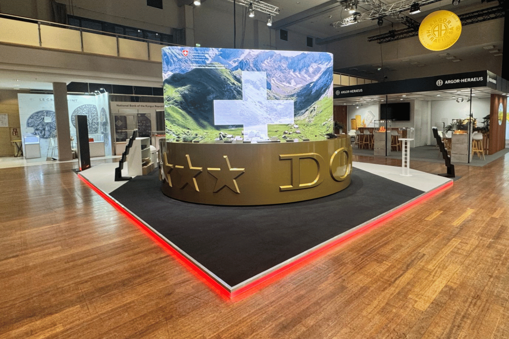 Messestand Swissmint mit großer, gebogener LED-Wand, goldener Theke und LED-beleuchtetem Messeboden.