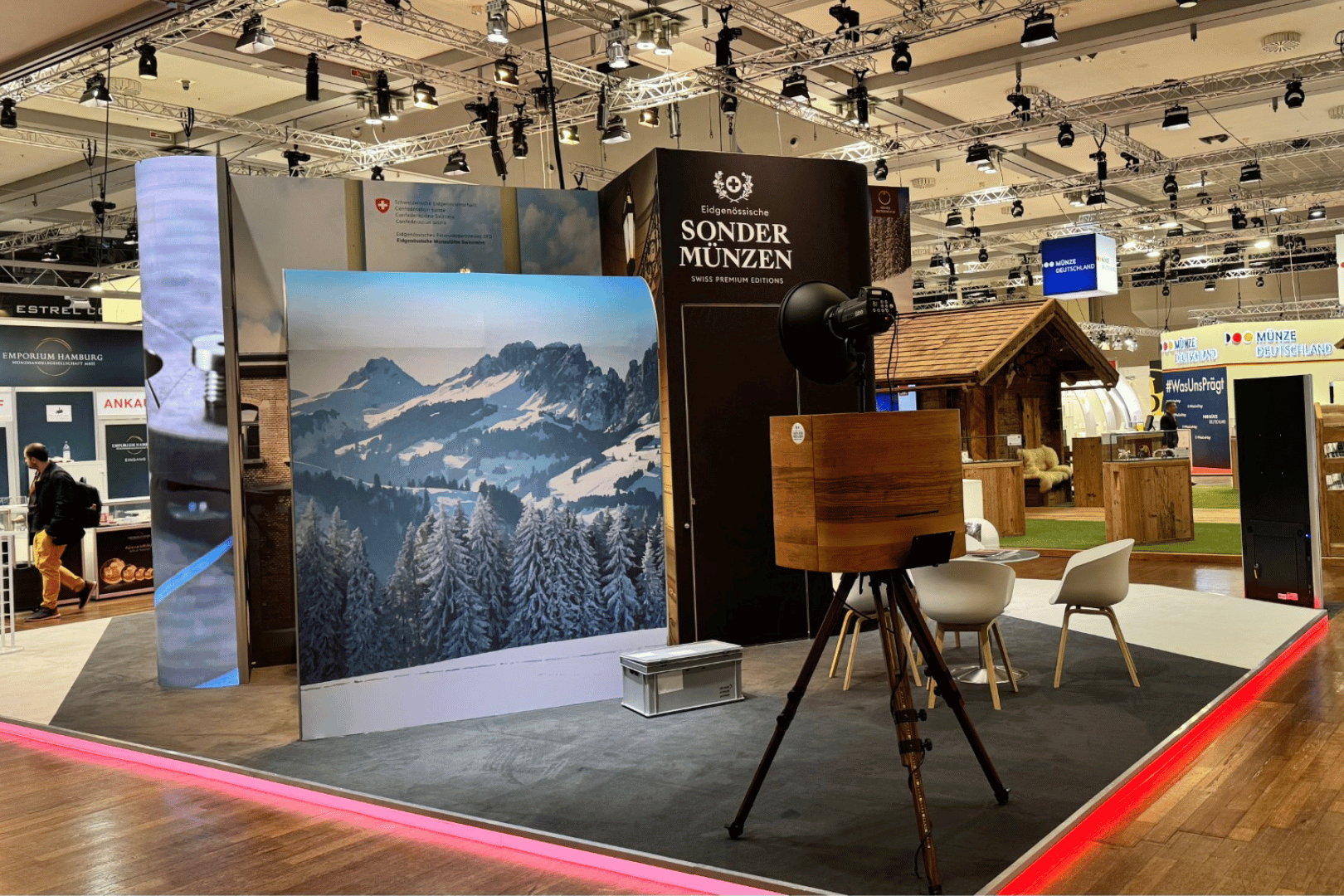 Beleuchtete Messewand mit Schweizer Bergpanorama und integrierten Sitzplätzen für Besucher.